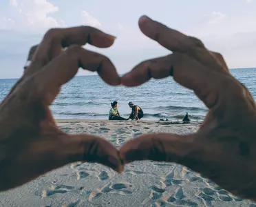 Hände, die um ein Urlauberpaar am Ostseestrand ein Herz formen