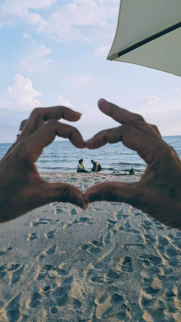 Hände, die um ein Urlauberpaar am Ostseestrand ein Herz formen