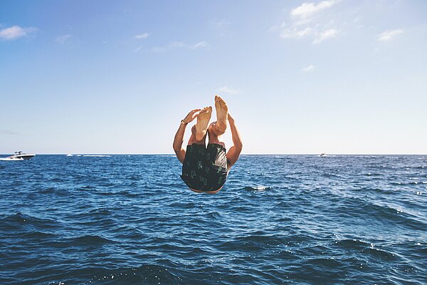 Junger Urlauber macht einen Salto über dem Meer